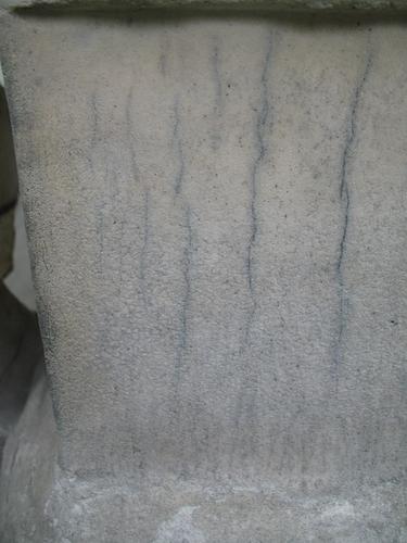 Трещины, загрязнения на поверхности мрамора. Колонии темноокрашенных грибов на поверхности камня. Нижняя часть саркофага под крестом.  Ровная вертикальная поверхность мрамора. Западная сторона памятника.